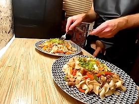 A naked gay chef prepares a dish of rice noodles with chicken and vegetables.
